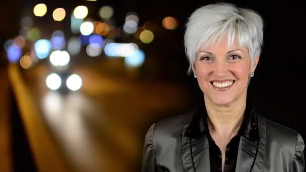 Business middle aged woman smiles - night city - night urban street with cars- car headlight - blurred-timelapse — Stock Video