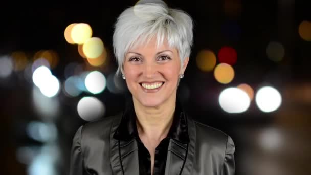 Affaires femme d'âge moyen sourit - ville de nuit - rue de nuit avec voitures - lampes - phare de voiture - flou doux — Video