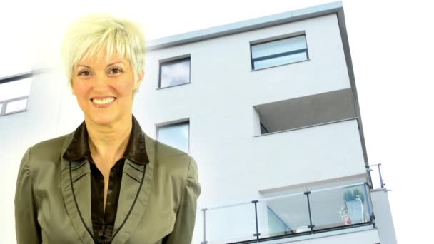 Mujer de mediana edad sonríe - edificio moderno - balcón - ventanas - naturaleza — Vídeos de Stock