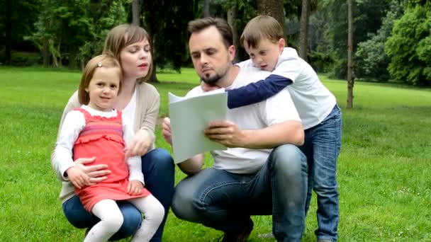 Familie (verliebtes mittleres Paar, nettes Mädchen und kleiner Junge) lesen Dokument im Park — Stockvideo