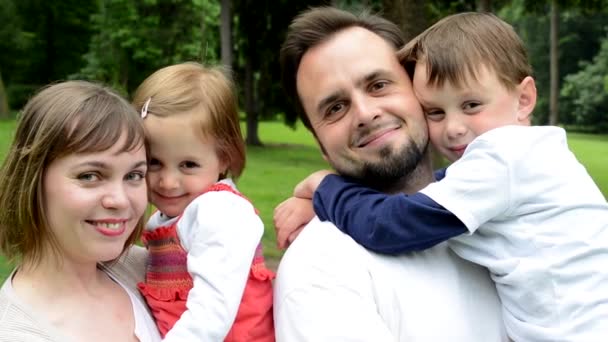 Familia (pareja en el medio del amor, linda chica y niño pequeño) sonrisa a la cámara en el parque — Vídeos de Stock