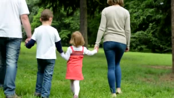 Family (middle couple in love, cute girl and small boy) walking in park from camera to distance — Stock Video