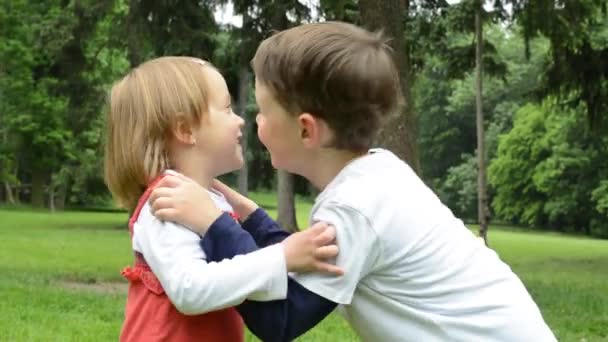 Children (siblings - boy and girl) give a kiss in park — Stock Video