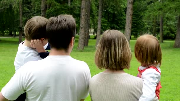 Family (middle aged couple in love, boy and girl) relax in park and point to distance - shot from back — Stock Video