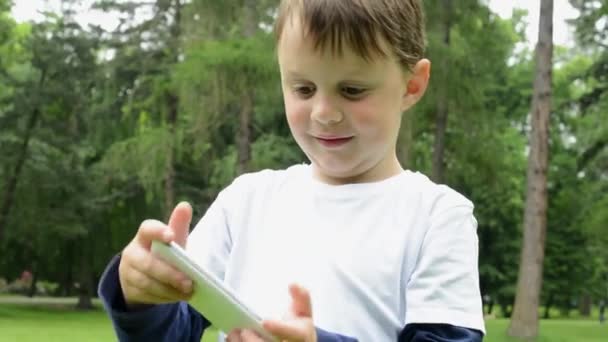 Young little boy plays games on smartphone - park — Stock Video