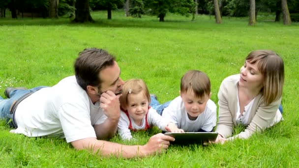 aile (aşık orta yaşlı çift, erkek ve kız) çim ve tablet üzerinde çalışmak yalan