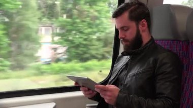 Genç yakışıklı hippi trenle seyahat eder ve tablet üzerinde çalışır - şehir - yakın plan