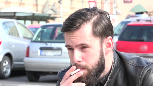 Jovem homem hipster bonito fuma um cigarro na rua carros estacionados no fundo — Vídeo de Stock