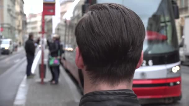 Jovem homem hipster bonito olhar em deixar o bonde da estação na cidade rua urbana com as pessoas — Vídeo de Stock