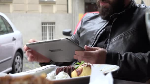 Young handsome hipster man works (typing) on smartphone - restaurant: outdoor seating - street with parked cars — 图库视频影像