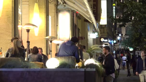 PRAGA, REPÚBLICA CHECA - 30 DE MAYO DE 2015: restaurante nocturno en la ciudad - asientos al aire libre - personas sentadas - calle urbana con gente caminando — Vídeo de stock