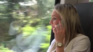 Genç ve çekici sarışın kadın trenle ve telefonuyla seyahat ediyor.