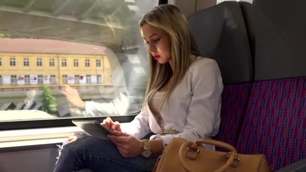 Jeune femme blonde attrayante voyageant en train et travaille sur tablette — Video