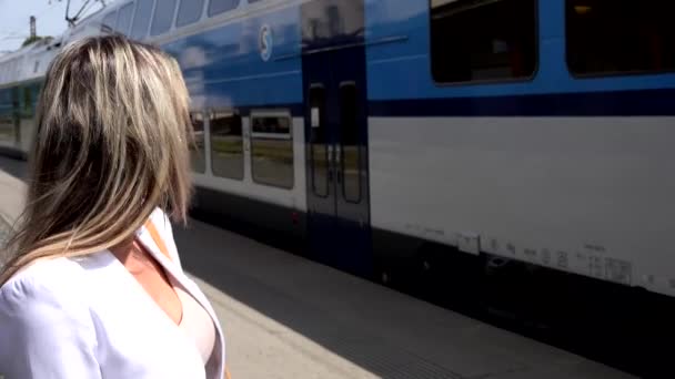 Jonge aantrekkelijke blonde vrouw wacht op station en vrouw kijkt vertrekkende trein vanaf het treinstation — Stockvideo