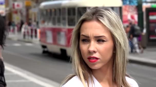 Молодая привлекательная блондинка оглядывается - городская улица в городе с трамваем на заднем плане - крупным планом лица — стоковое видео