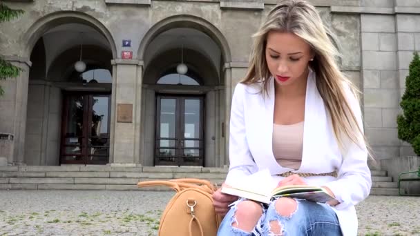 Jong aantrekkelijk blond vrouw leest boek in de voorkant van universiteit — Stockvideo