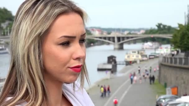 Молодая привлекательная блондинка оглядывается вокруг - мосты с рекой - прогулочные люди - крупным планом лица — стоковое видео
