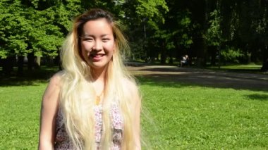 Genç, çekici, mutlu Asyalı kadın parkın güneşli gününün tadını çıkarıyor. Kameraya gülümsüyor.