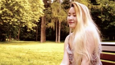 Genç Asyalı çekici mutlu kadın parkta bankta oturur - parkın etrafına bakın - yakın plan - filtre