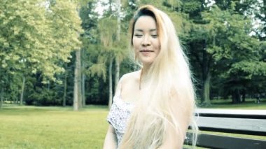 Genç Asyalı çekici mutlu kadın parkta bankta oturur - kameraya gülümser - yakın plan - filtre