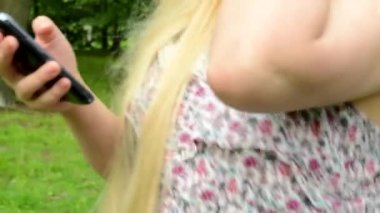Genç bir kadın parkta akıllı telefonuyla yürüyor ve çalışıyor. Detay: Steadicam