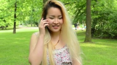 Genç Asyalı çekici kadın parkta yürür ve telefon eder - Steadicam