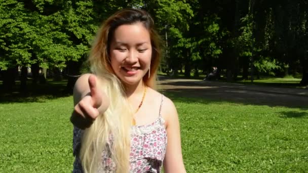 Genç, çekici, mutlu Asyalı kadın parkta baş parmağını gösteriyor. Kameraya gülümsüyor. — Stok video