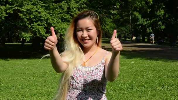 Junge attraktive glückliche asiatische Frau zeigt Daumen nach oben im Park - aus nächster Nähe — Stockvideo