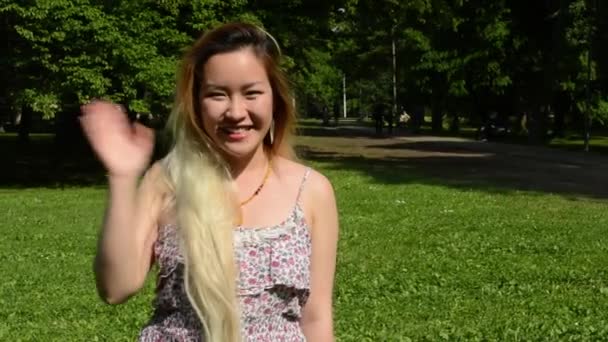 Jovem atraente asiático feliz mulher entusiasticamente ondas no parque - close-up — Vídeo de Stock