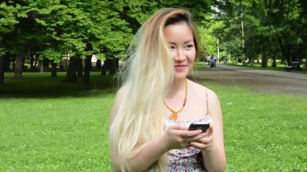 Молодая привлекательная счастливая азиатка пишет сообщение в парке - крупным планом — стоковое видео