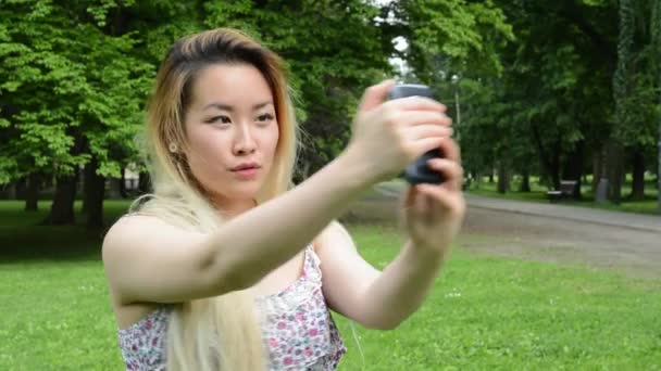 Ung attraktiv glad asiatisk kvinna skjuter sig själv i parken - selfie — Stockvideo