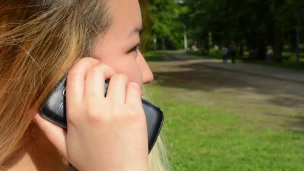 Joven asiático atractivo feliz mujer teléfonos con alguien en el parque - mirar desde un lado - detalle — Vídeo de stock