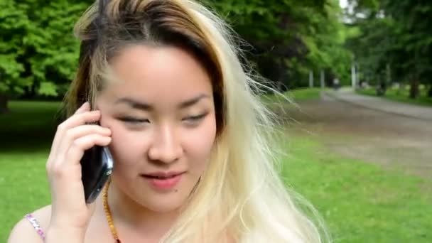 Young asian attractive happy woman phones with somebody in the park - windy - detail — Stock Video