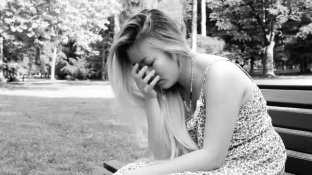 Mladá asijská atraktivní smutná žena sedí na lavičce v parku - černá a bílá — Stock video