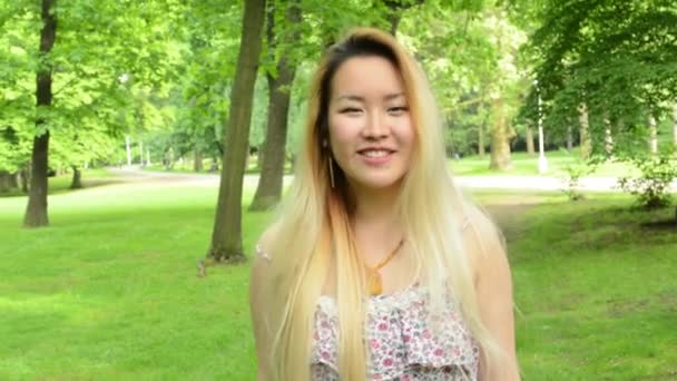 Young attractive happy asian woman turns over and smiles in the park - smiles to camera — Stock Video