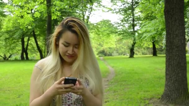 Молода приваблива щаслива азіатка повертається і посміхається в парку посміхається камері — стокове відео