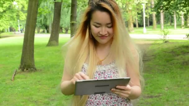 Young asian attractive woman uses tablet - walks in the park - steadicam — Stock Video