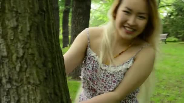 Jonge aantrekkelijke vrouw verstopt zich achter de bomen en loopt - steadicam — Stockvideo