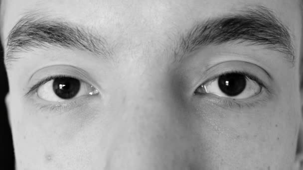 Молодой человек открывает глаза и моргает без эмоций - черно-белый фильтр — стоковое видео