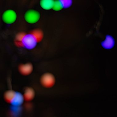 Bokeh ışıkları rengarenk çelenk ışıkları bulanıklaştırdı. Yeni yıl ya da doğum günü kutlaması. Siyah üzerine çok renkli arka plan ışığı.