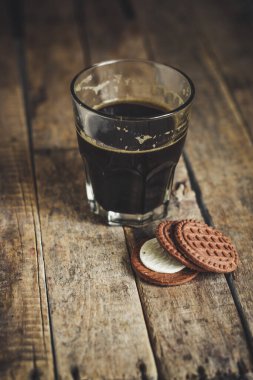 Tahta zemin üzerinde kurabiyeler olan bir bardak kahve. 