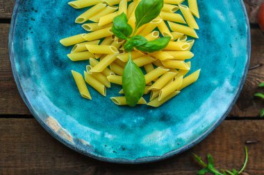 Tahta arka planda fesleğenli ve yeşil yapraklı makarna.