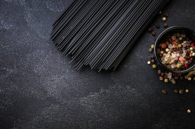 Siyah arka planda baharat ve otlarla pişirilmemiş siyah spagetti manzarası. en üstteki görünüm.