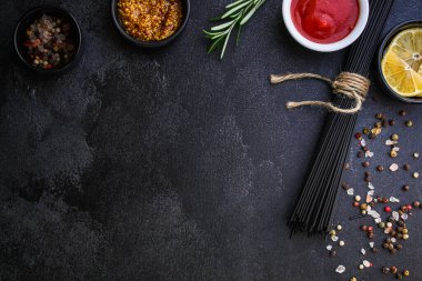 Siyah arka planda baharat ve otlarla pişirilmemiş siyah spagetti manzarası. en üstteki görünüm.