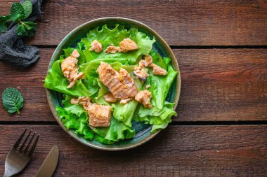 Salata yapraklarının üzerinde konserve somon dilimleri.