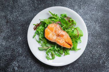 Arugula soslu somon bifteği ve tabakta salata yaprakları. en üstteki görünüm.