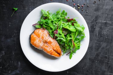 Arugula soslu somon bifteği ve tabakta salata yaprakları. en üstteki görünüm.