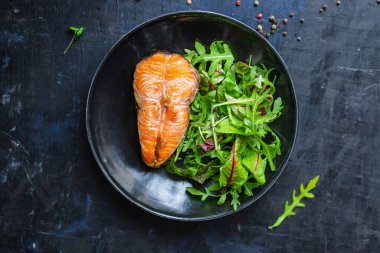 Arugula soslu somon bifteği ve tabakta salata yaprakları. en üstteki görünüm.