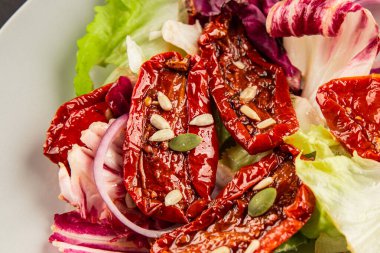 Salata, kurutulmuş domates, yeşil yaprak, soğan, doğal ürün, lezzetli aperatif. Lezzetli gurme yemek arkaplanı, masa, rustik üst manzara, fotokopi alanı, vejetaryen diyeti ve vejetaryen yemeği.