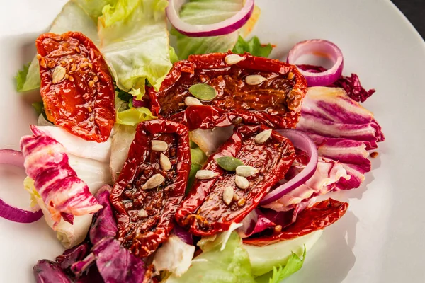 Salata, kurutulmuş domates, yeşil yaprak, soğan, doğal ürün, lezzetli aperatif. Lezzetli gurme yemek arkaplanı, masa, rustik üst manzara, fotokopi alanı, vejetaryen diyeti ve vejetaryen yemeği.